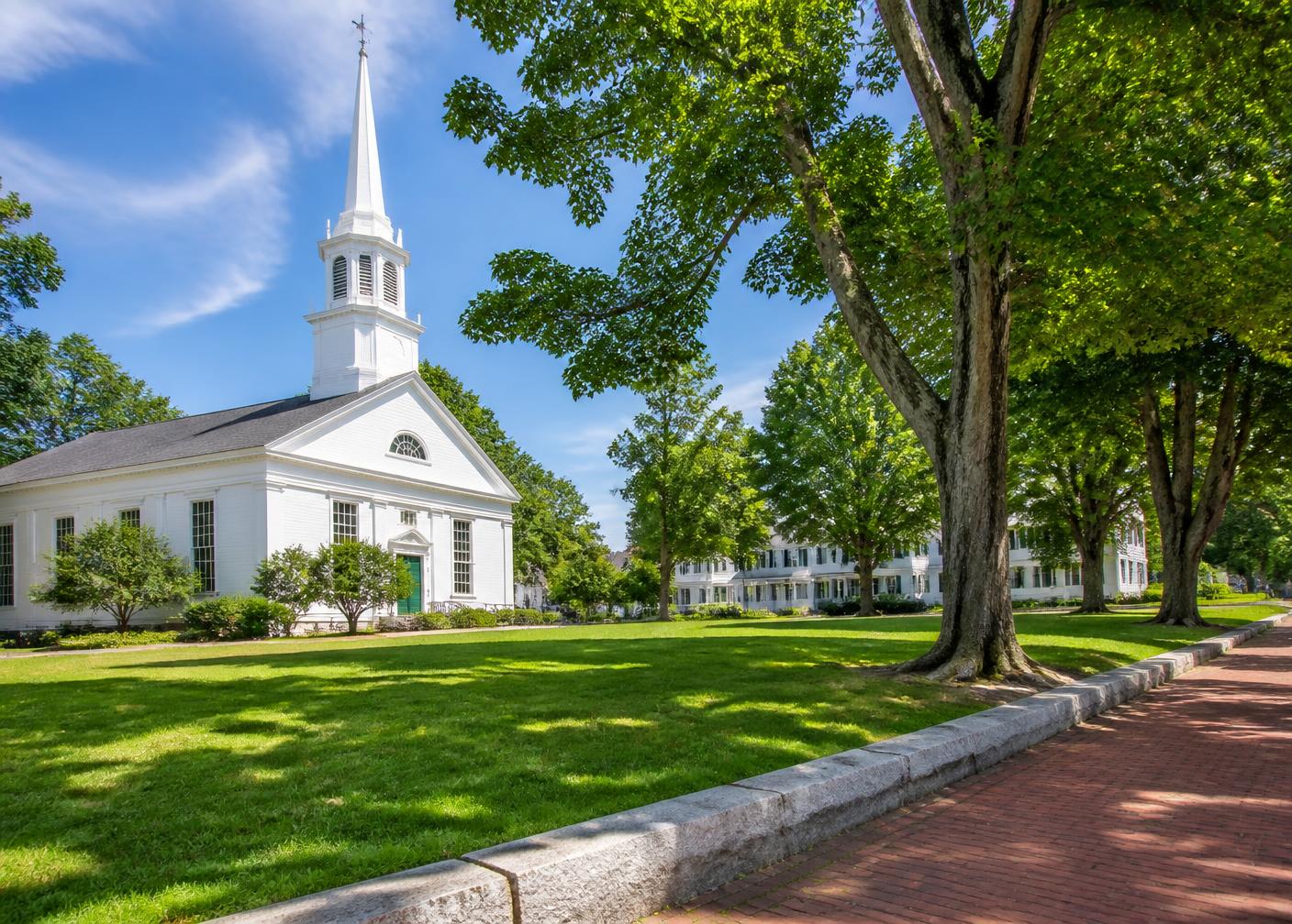 New England town common with a white steepled meeting house, shade trees and a brick sidewalk
