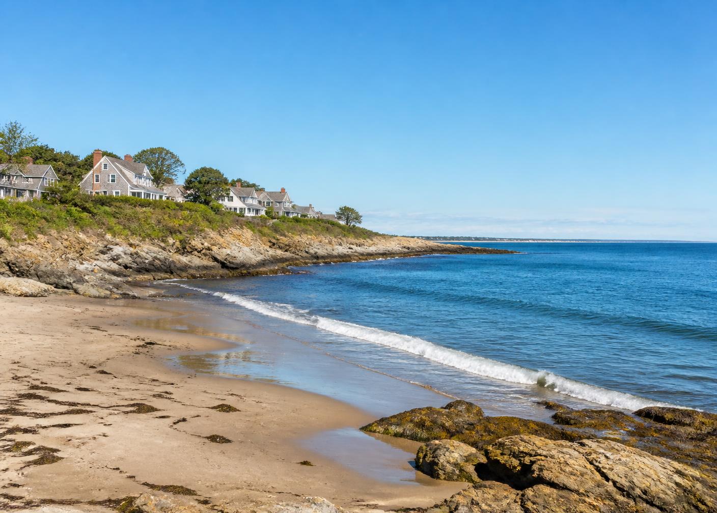 Sandy beach and rocky shoreline on the New Hampshire seacoast with shingled coastal homes above the bluff